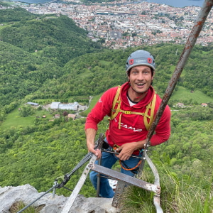 Christial Bickel mit rotem Camp-Pullover und grau-rotem Kletterhelm steht an einer Leiter im Klettersteig.