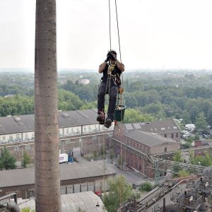 Ein Kletterer klettert am Seil einen Industrieturm hinauf.