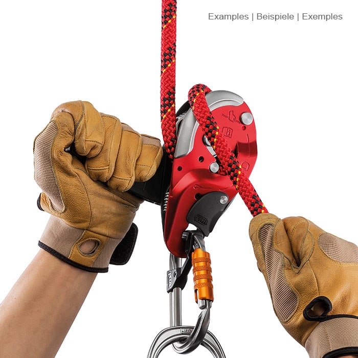 I'D L von Petzl, das Klettergerät wird von zwei Händen mit braunen Handschuhen gehalten, ein rotes Seil ist eingefädelt und ein Karabiner hängt unten