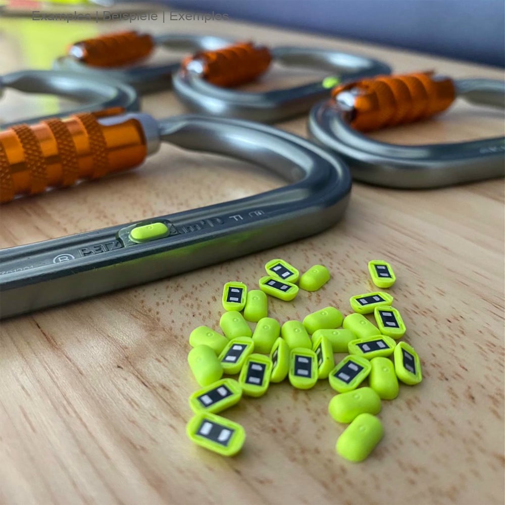 Hardware NFC Tag von Scannable, viele kleine gelb-grüne NFC Tags liegen auf einem Holztisch vor mehreren Karabinern mit orangem Verschluss