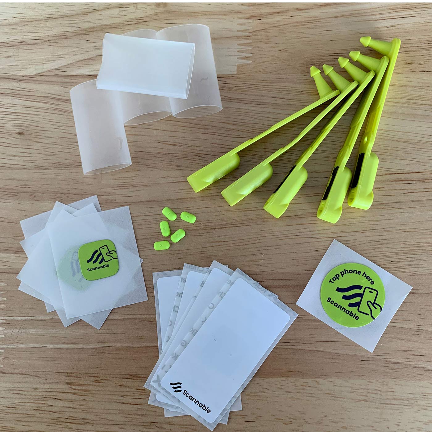 Climber Pack NFC Tag mit gelben Kunststoffteilen, mehreren weißen Hüllen, grünen Aufklebern mit Scannable-Logo und kleinen gelben Komponenten auf einem Holztisch