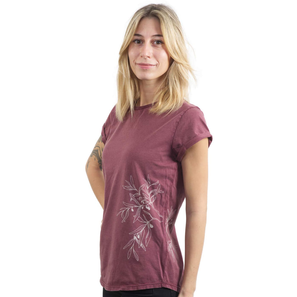 Eine Frau trägt ein bordeauxrotes T-Shirt "Olive Branch" mit weißem Olivenzweig-Motiv an der Seite und hat die Hände hinter dem Rücken.
