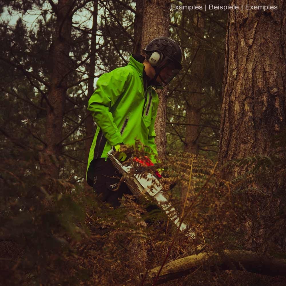 Person trägt grüne BreatheDry Smock Jacke mit schwarzer Hose und Helm im Wald, hält eine Motorsäge
