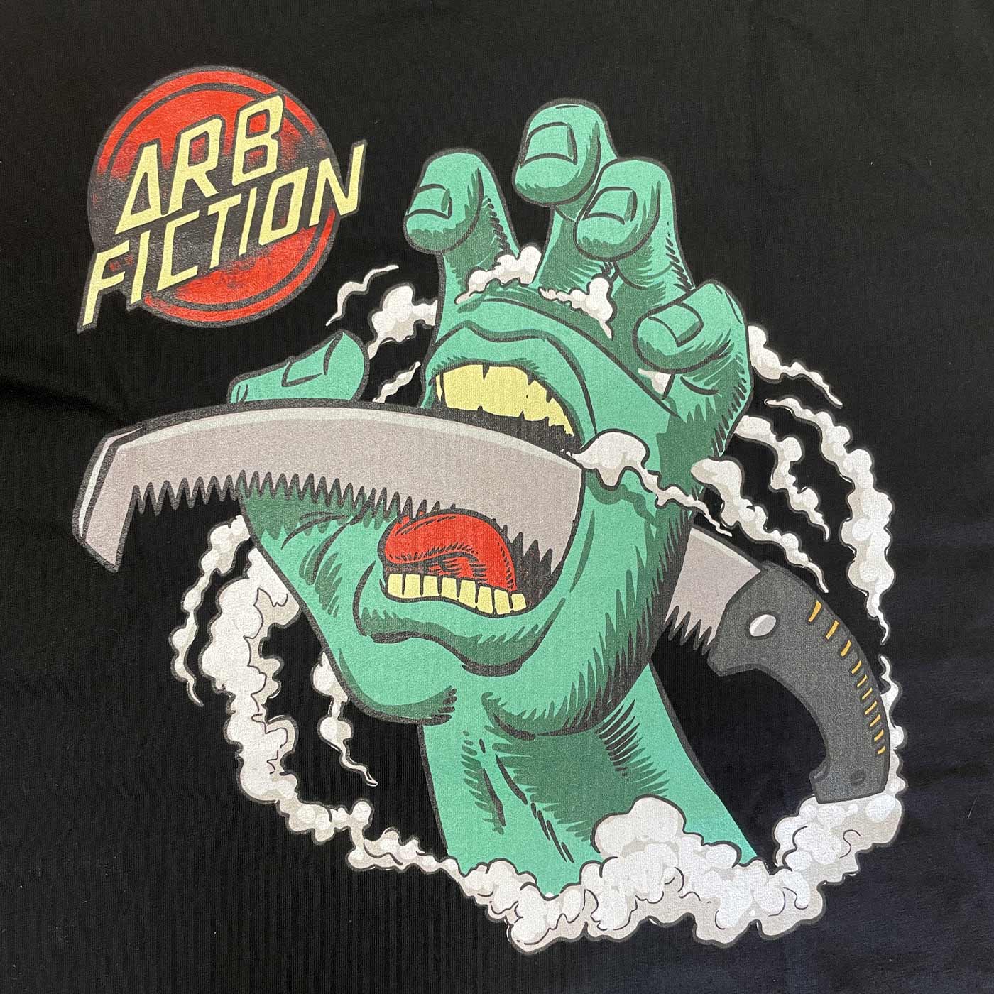 Nahaufnahme des Aufdrucks auf dem schwarzen T-Shirt mit grüner Hand, Säge und rotem "ARB FICTION"-Logo, Produktname Screaming Hand