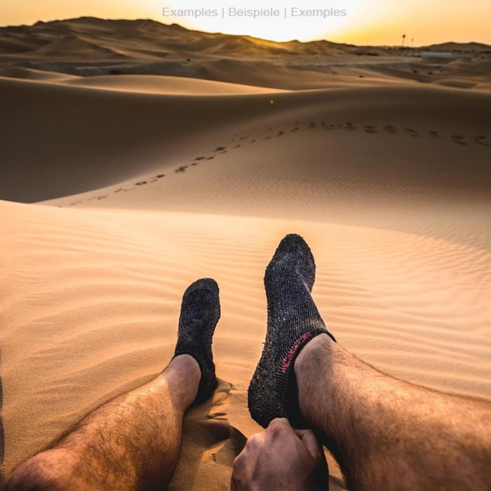 Skinners schwarze Socke mit gummierter Sohle an einem Fuß in der Wüste, im Hintergrund Sanddünen bei Sonnenuntergang