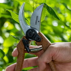 Berger C1200 Gartenschere mit braunen Griffen und silberner Klinge, Marke Berger, Modell C1200, gehalten von einer Hand vor grünem Blattwerk