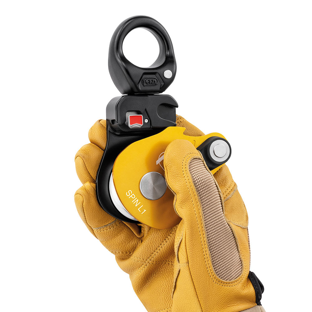 Petzl Spin L1 Seilrolle mit gelbem Gehäuse, gehalten von einer Hand mit gelbem Arbeitshandschuh