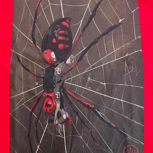 Nahaufnahme des Spinnenaufdrucks auf dem roten ART Spider Shirt, die Spinne hat schwarze und rote Farben und sitzt auf einem weißen Spinnennetz auf dunklem Hintergrund