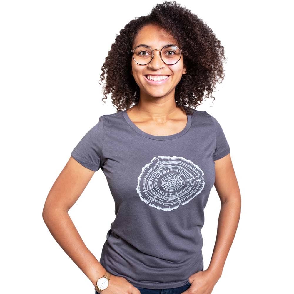 Eine Frau mit lockigen dunklen Haaren und Brille trägt ein graues Treeslice Women T-Shirt mit weißem Baumstammschnitt-Design auf der Vorderseite