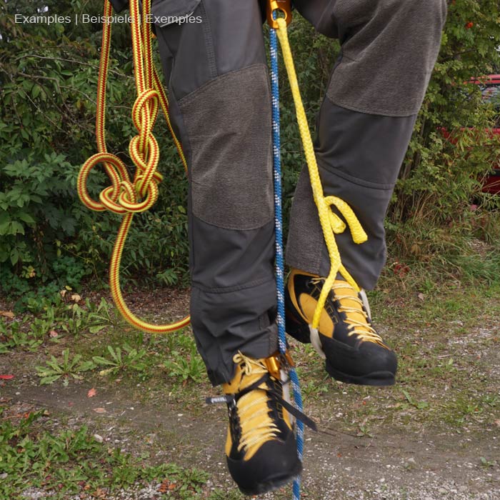 Bungeetool in Blau mit elastischem, gewelltem Abschnitt und flachem Gurtband mit schwarzem Rand und grünem Innenstreifen an grauer Outdoorhose mit gelb-schwarzen Bergschuhen und mehreren Kletterseilen