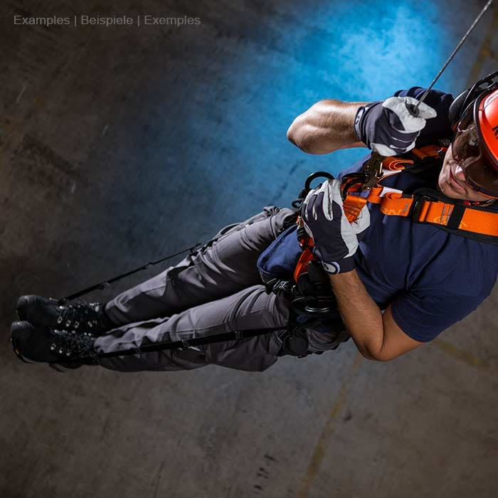 Relief Straps, Person in Schutzhelm und Handschuhen trägt orangefarbenen Sicherheitsgurt beim Abseilen in dunkler Umgebung