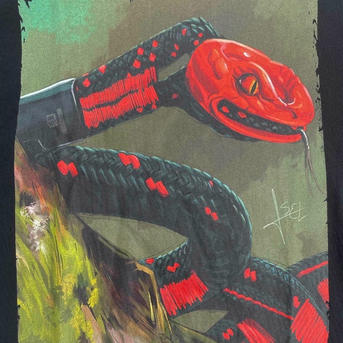 Nahaufnahme des farbigen Schlangendesigns auf dem schwarzen ART Snake Shirt mit roten und schwarzen Details und einer grünen Hintergrundfläche