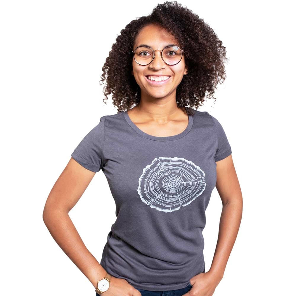 Eine Frau mit lockigen dunklen Haaren und Brille trägt ein graues Treeslice Women T-Shirt mit weißem Baumstammschnitt-Design auf der Vorderseite