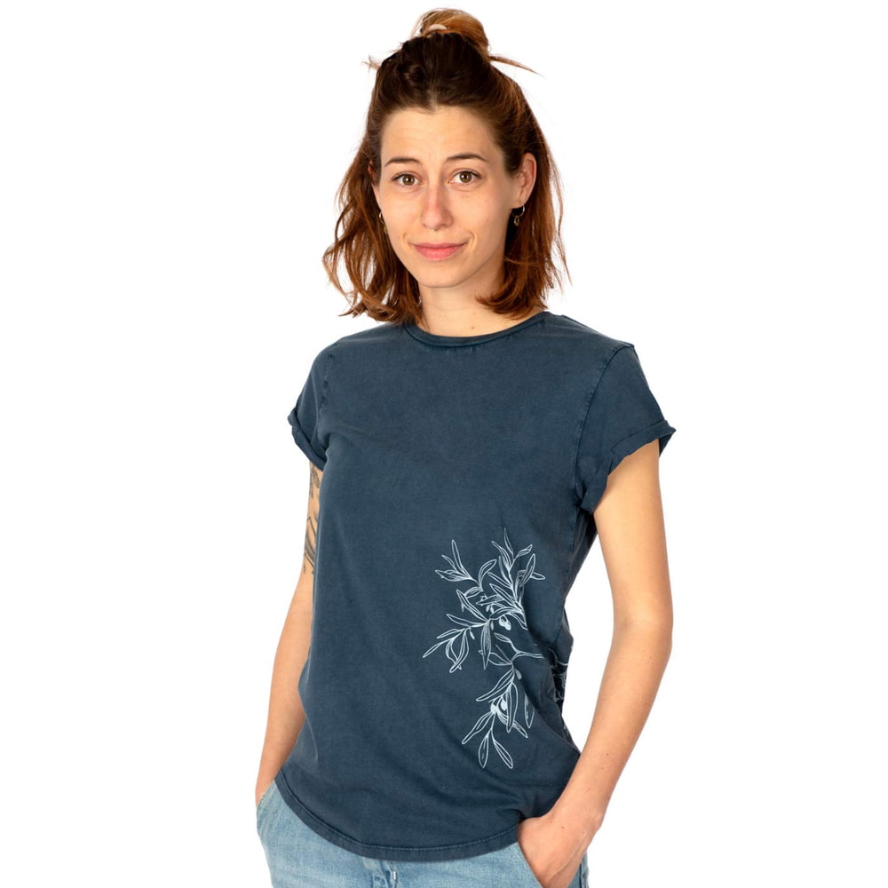 Eine Frau trägt ein dunkelblaues T-Shirt "Olive Branch" mit weißem Olivenzweig-Motiv an der Seite und hat die Hände in den Hosentaschen.