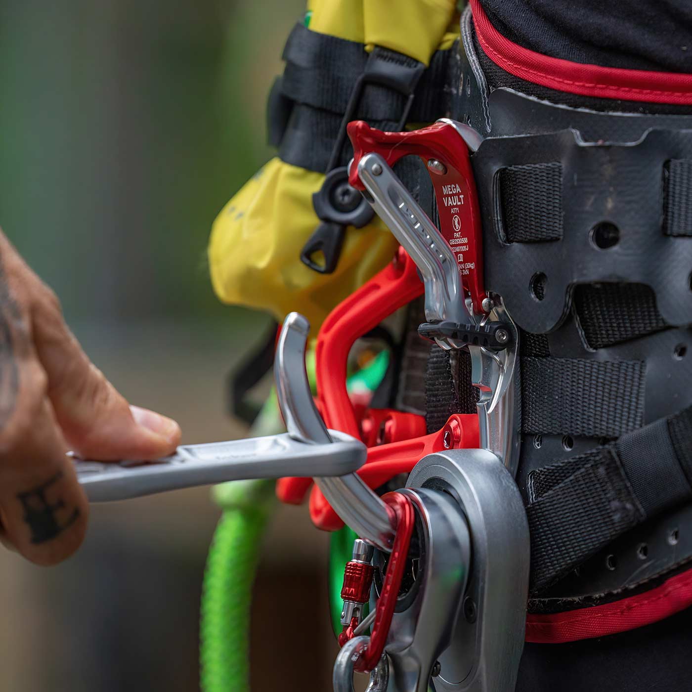 Nahaufnahme einer Hand, die den Mega Vault Karabiner in Silber und Rot an einem schwarzen und roten Gurt bedient