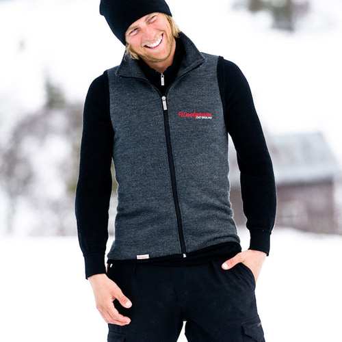 Vest 400, graue ärmellose Weste mit Reißverschluss, getragen von einem lächelnden Mann mit schwarzer Mütze und schwarzem Unterziehshirt, rotes Woolpower Östersund Logo auf der Brust