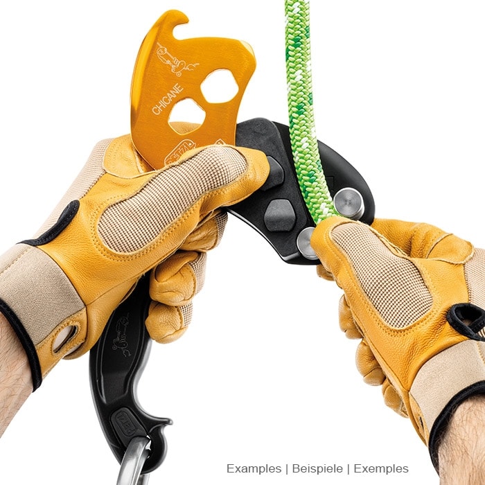Petzl Chicane, gelb-schwarzes Sicherungsgerät mit Griff, gehalten von zwei Händen mit gelben Handschuhen an einem grünen Seil