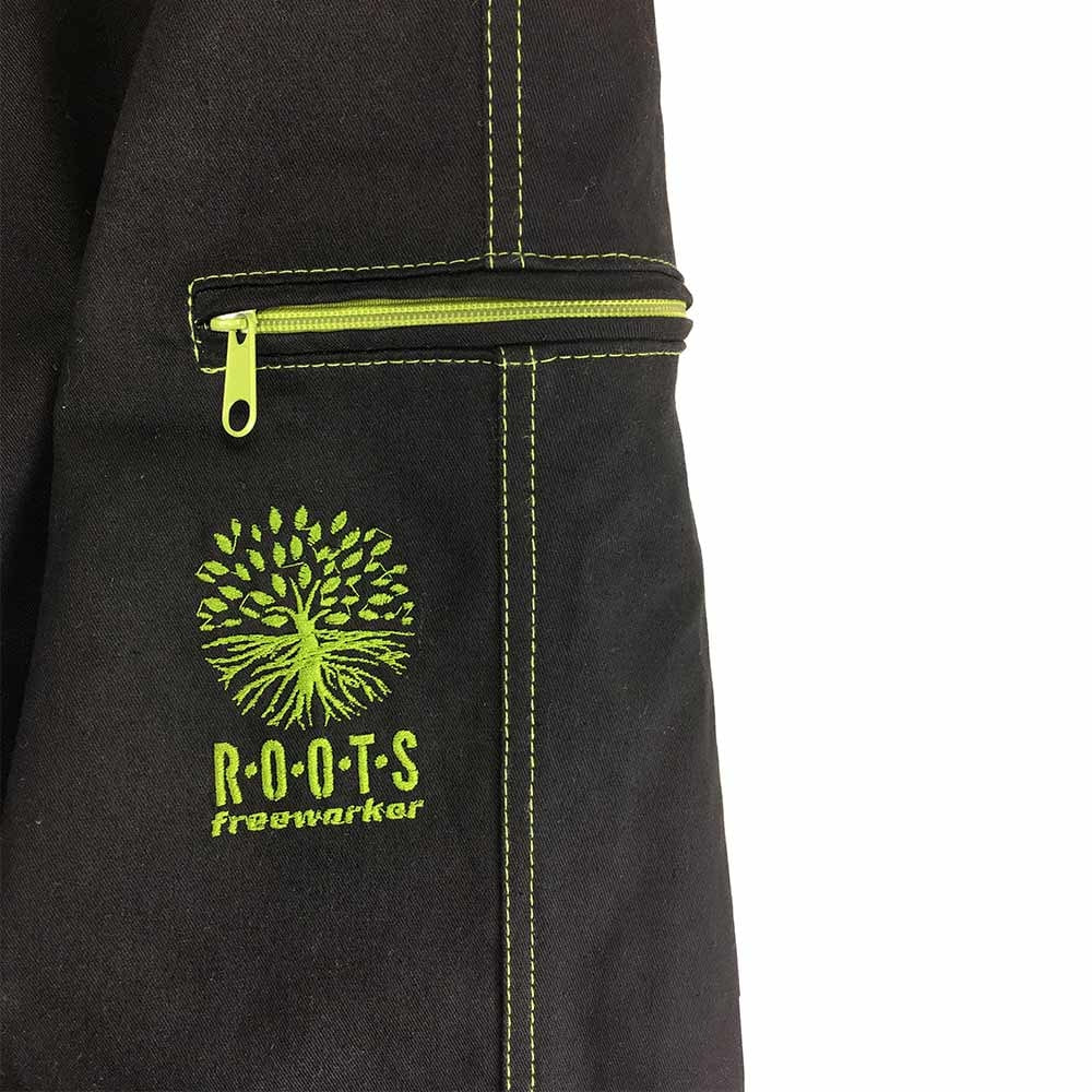 Nahaufnahme einer Tasche der Roots Pure Outdoorhose in Schwarz mit grünem Reißverschluss und grüner Naht, grüne Stickerei eines Baums mit Schriftzug "ROOTS freeworker"