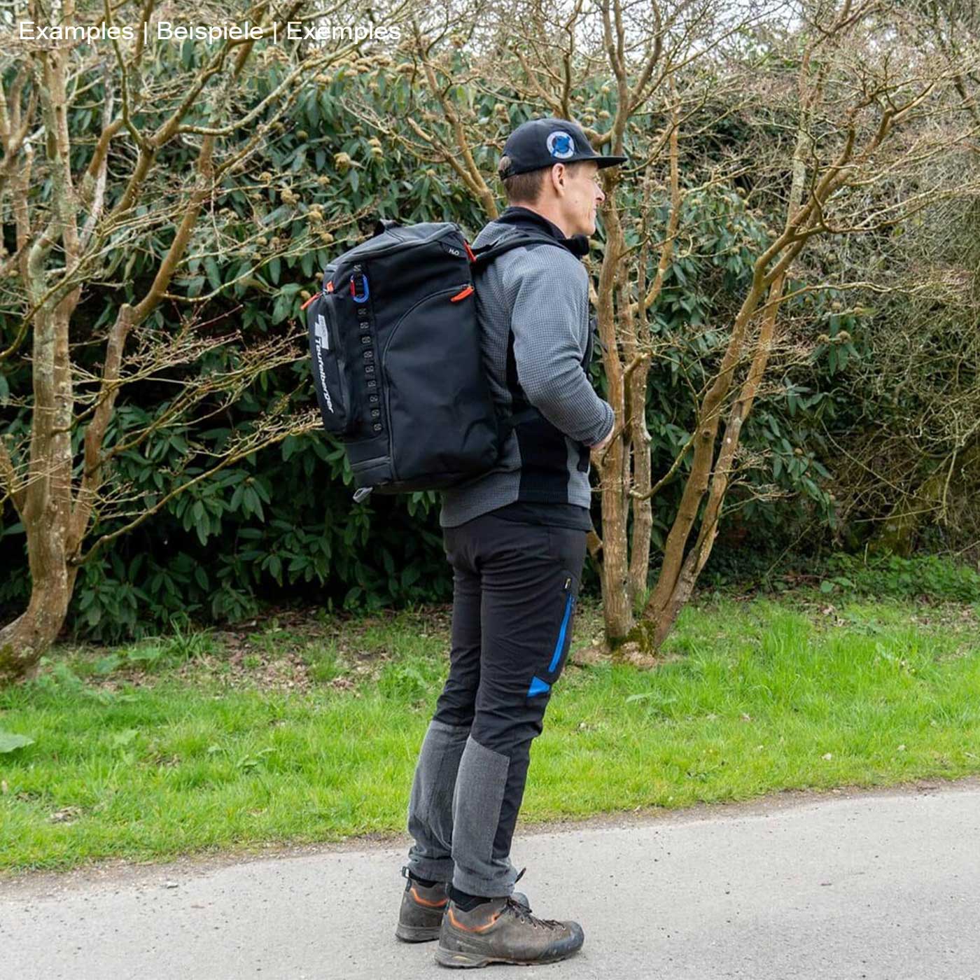 Person mit schwarzem Rucksack Baby Mule, Hersteller nicht sichtbar, steht seitlich auf einem Weg, umgeben von Bäumen und Gras