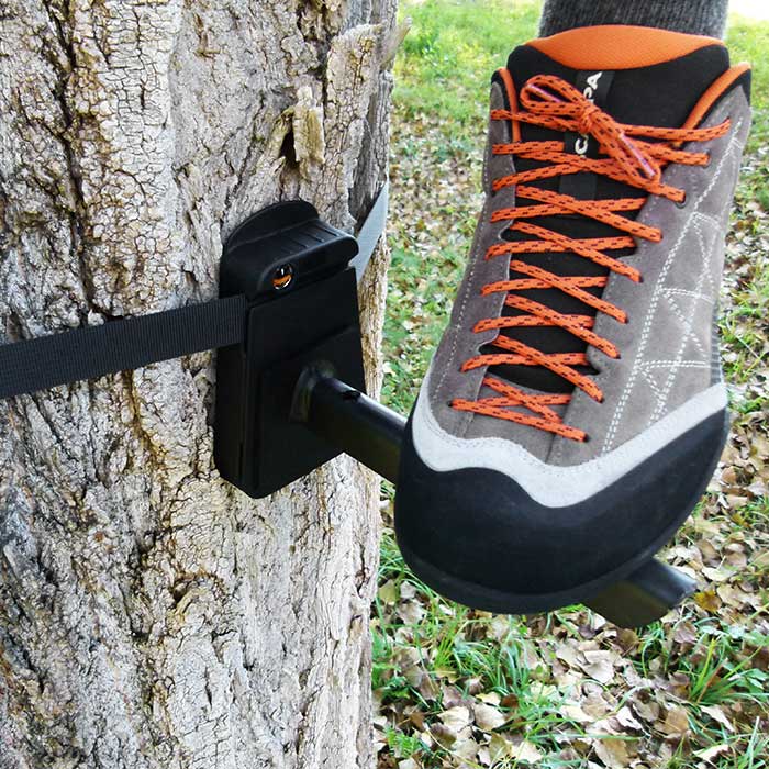 Tree-Monkey Steppers schwarzer Metallfuß mit schwarzem Befestigungsblock an Baumstamm befestigt, grauer Schuh mit orangenen Schnürsenkeln auf Metallfuß