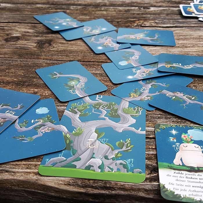 Kodama – Die Baumgeister mehrere Spielkarten mit Baumillustrationen auf Holztisch ausgelegt, Kosmos Herstellername nicht sichtbar