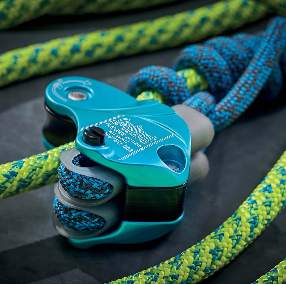 Flexbee Nahaufnahme des blauen Sicherungsgeräts mit blau-gelbem Kletterseil auf schwarzem Untergrund