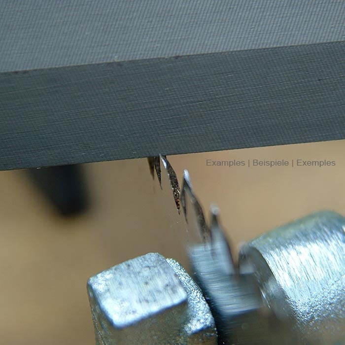 Nahaufnahme einer grauen Feile, die an der Kante einer Metallfläche geschärft wird