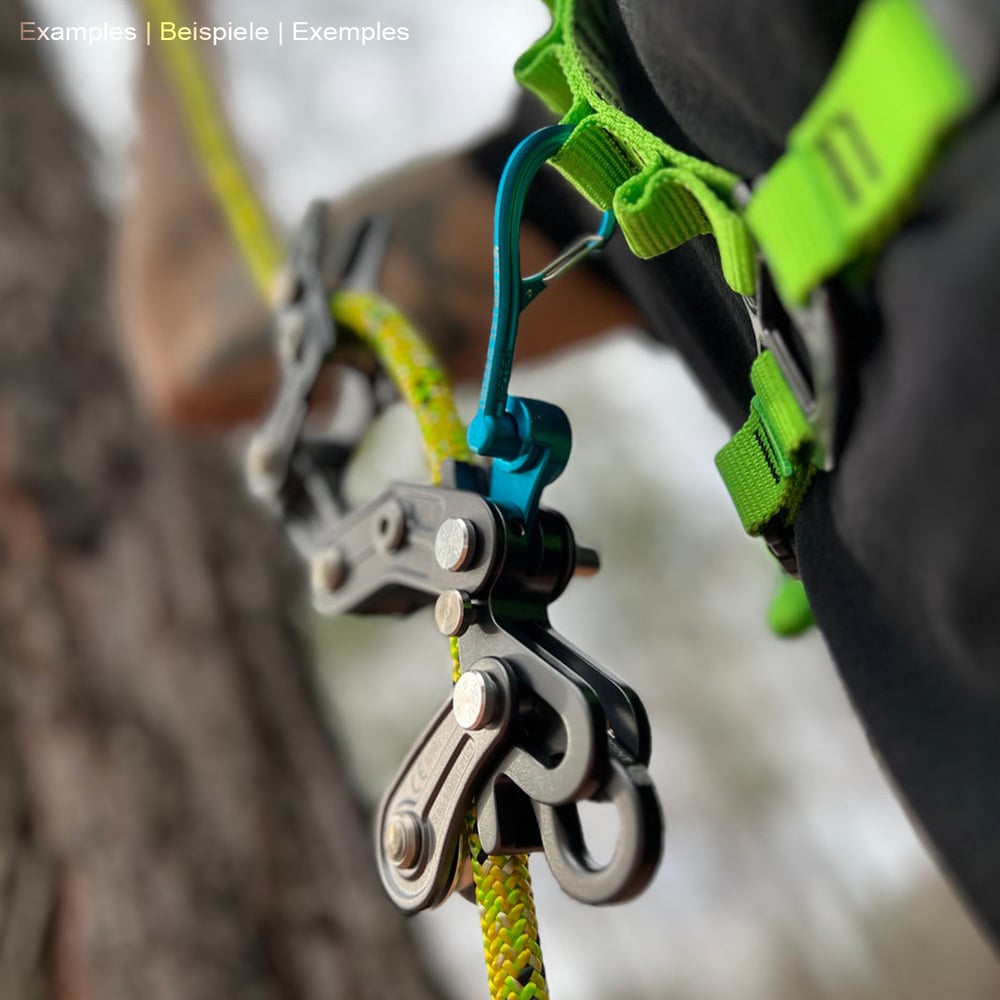Person mit grünem Klettergurt, an dem ein blauer Magneato Karabinerhaken befestigt ist, der mit einem schwarzen Klettergerät und gelbem Seil verbunden ist, im Freien an einem Baum.