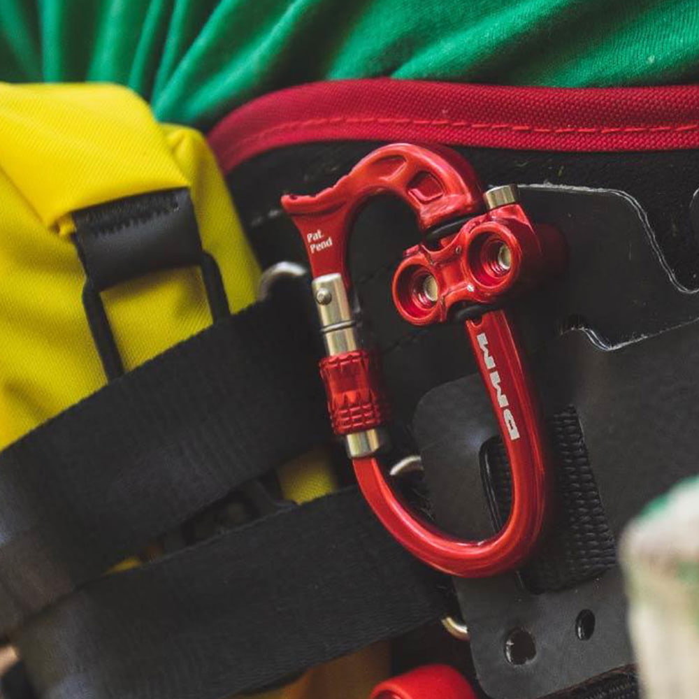 Micro Vault von DMM, roter Karabiner mit Schraubverschluss an einem schwarzen Rucksackriemen befestigt