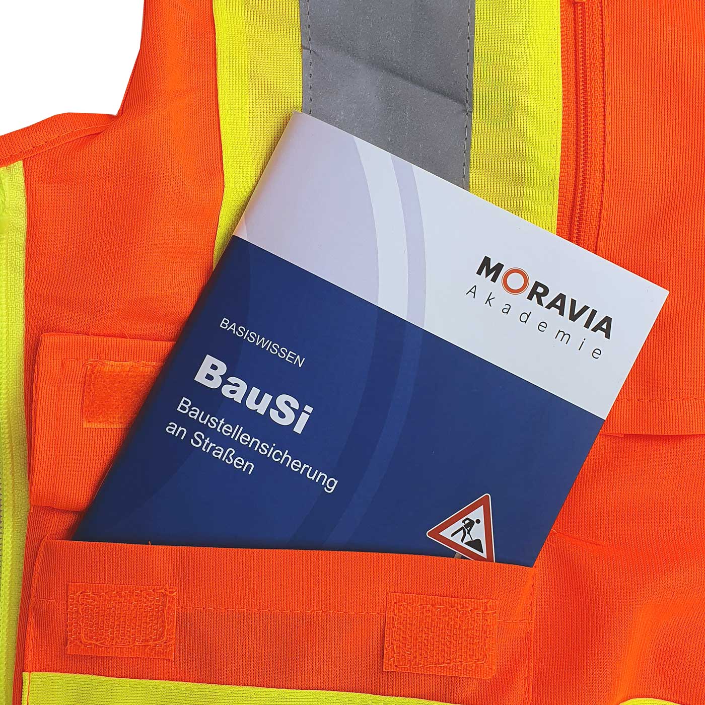 Buch BauSi von Moravia Akademie in der Tasche einer orangefarbenen Warnweste mit gelben und grauen Reflexstreifen