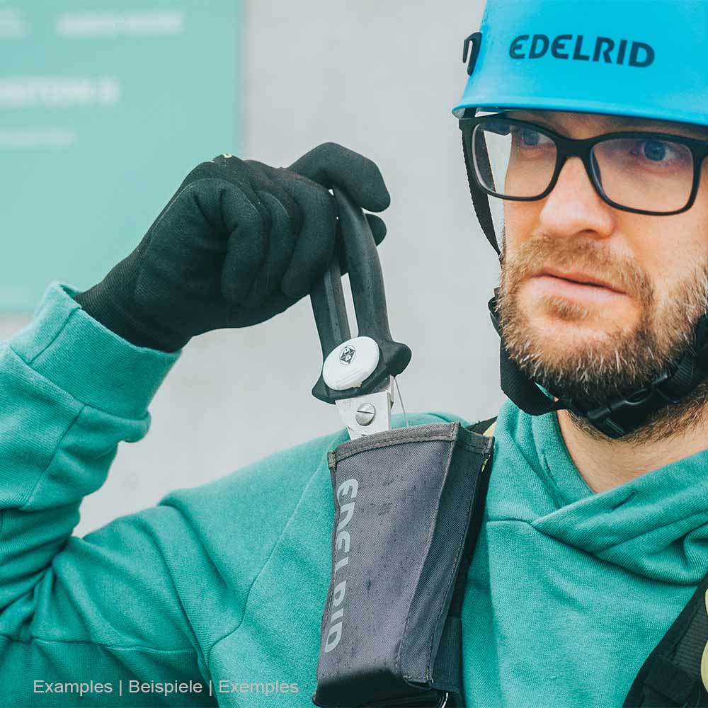 Mann mit blauer Edelrid-Schutzhelm und grüner Jacke hält eine schwarze Schere aus dem schwarzen Edelrid Rescue Holster von Edelrid