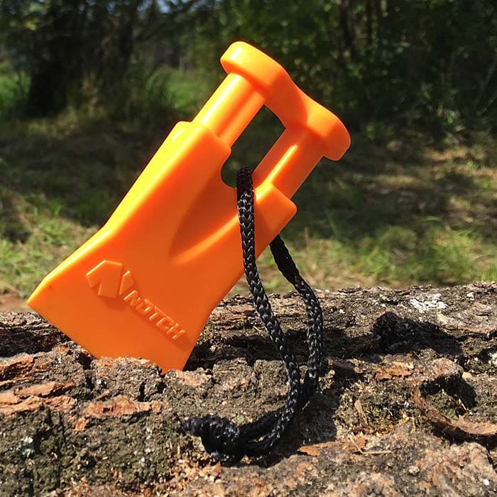 Climbers Best Friend Wedge von Notch, orangefarbener Kunststoffkeil mit schwarzer Schnur liegt schräg auf Baumrinde im Freien